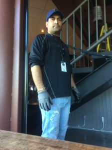Hadi Akhoondzade (he/him) URSU Maintenance Coordinator stands next to a stairwell indoors at The Lazy Owl.